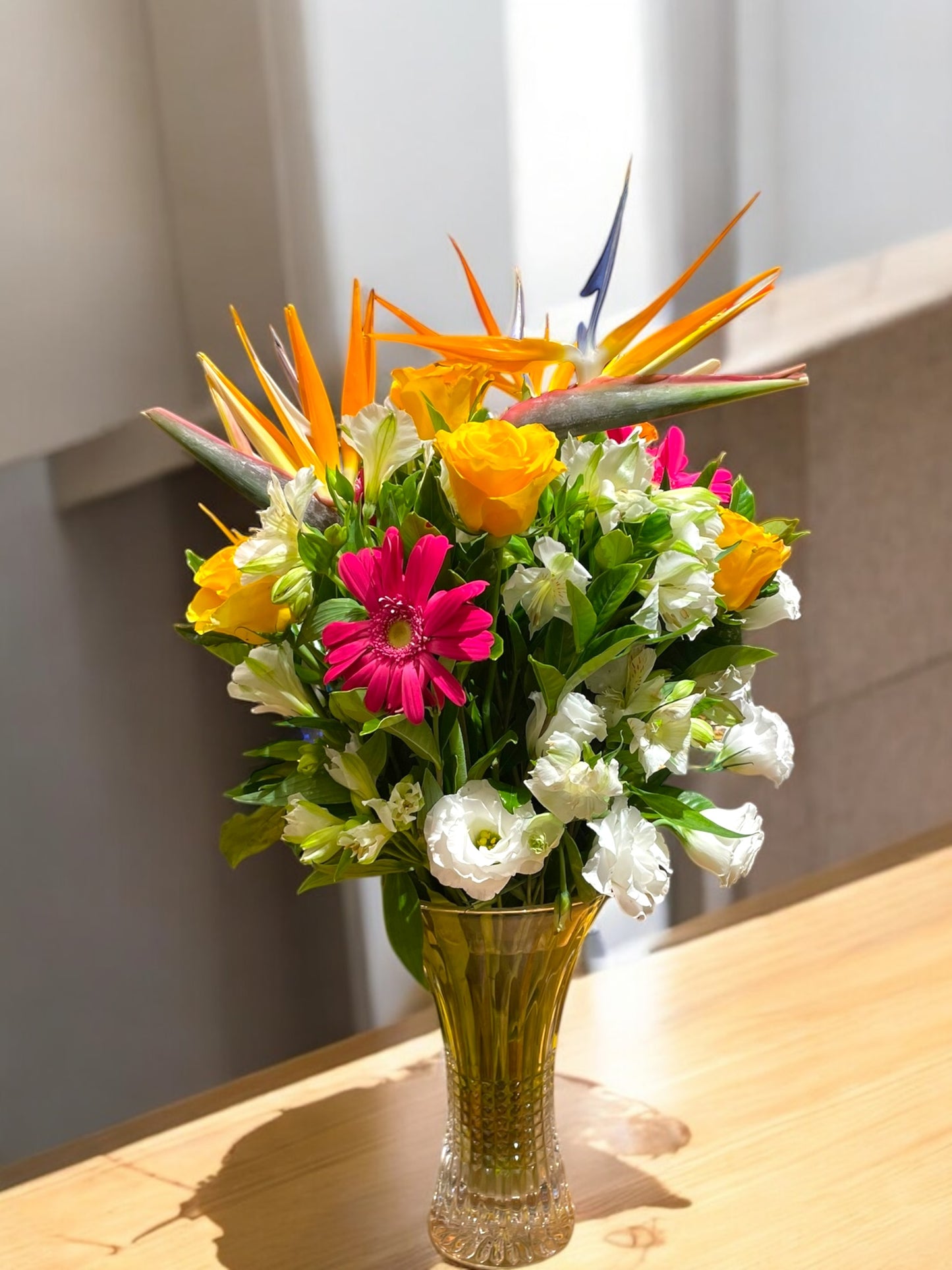 Tropical arrangement with Bird of Paradise, Roses and Lisianthus in a glass vase.
