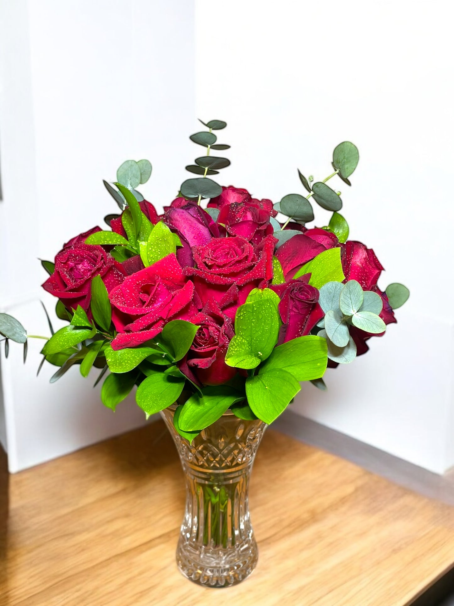 Luxurious bouquet with 24 natural red roses and eucalyptus in a glass vase.