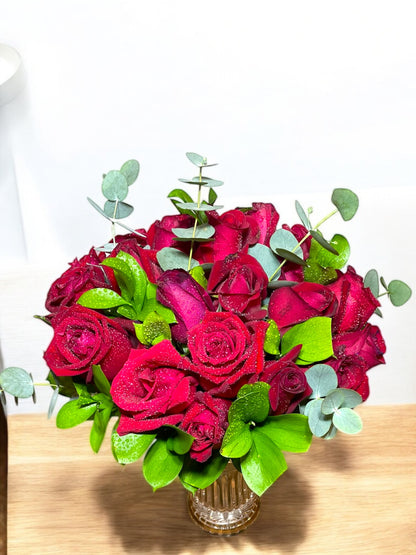 Luxurious bouquet with 24 natural red roses and eucalyptus in a glass vase.