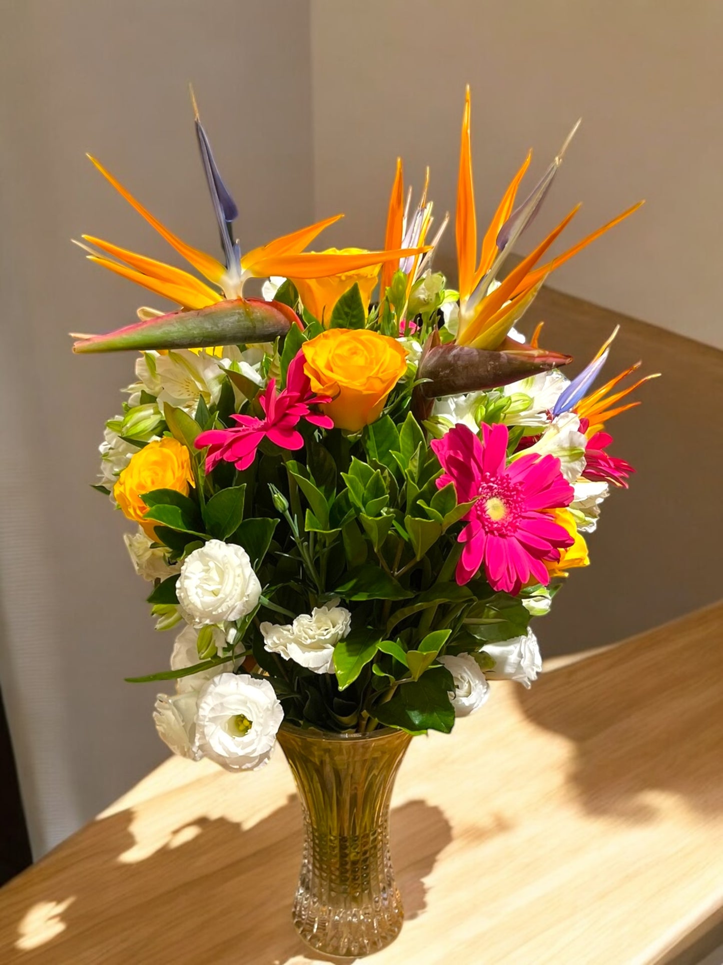 Tropical arrangement with Bird of Paradise, Roses and Lisianthus in a glass vase.